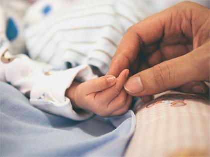 Vauvan ja aikuisen käsi koskettavat hellästi toisiaan. Tunnelma on lämmin.