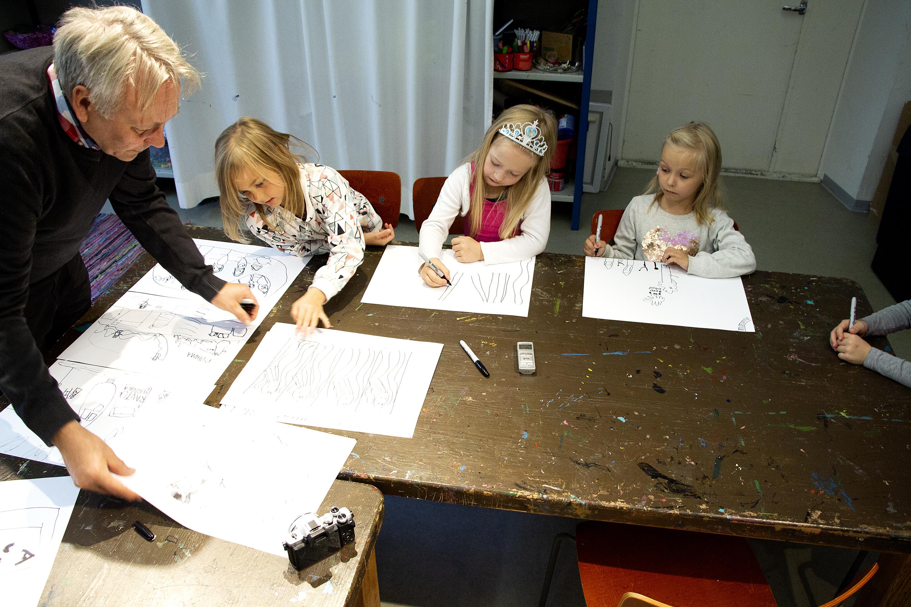 Pöydän ääressä istuu neljä esikoululaista ja AIMO-koulun rehtori Pekka Lehtimäki käy läpi lasten piirrustuksia.